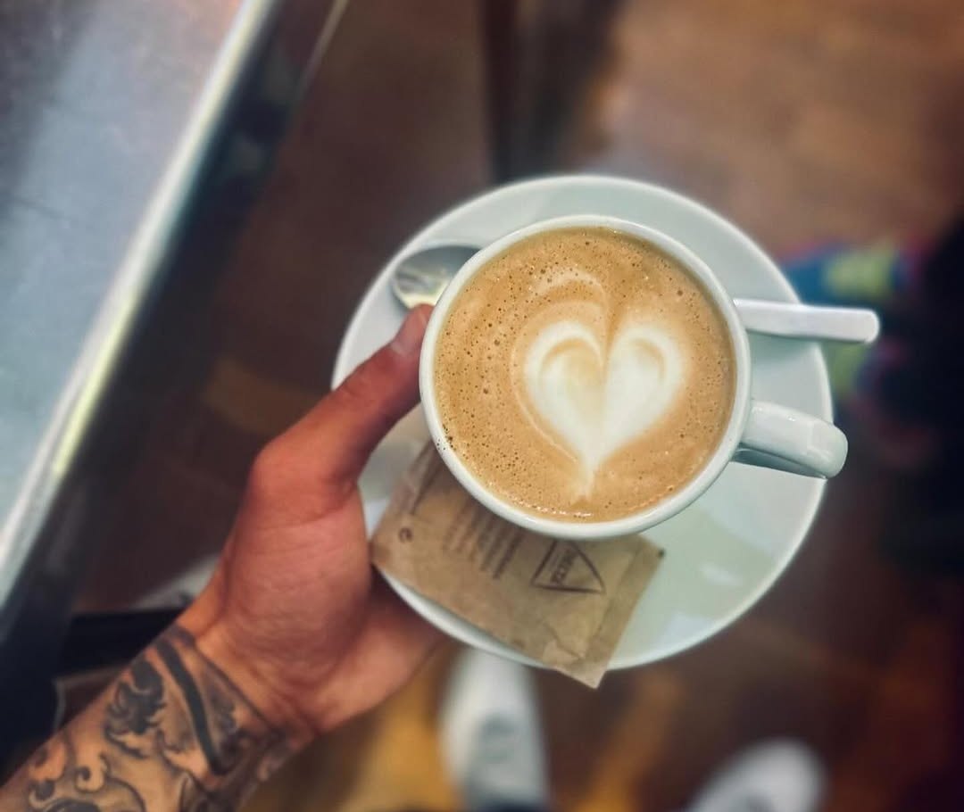Mão a segurar uma chávena de café com leite com um coração desenhado na espuma